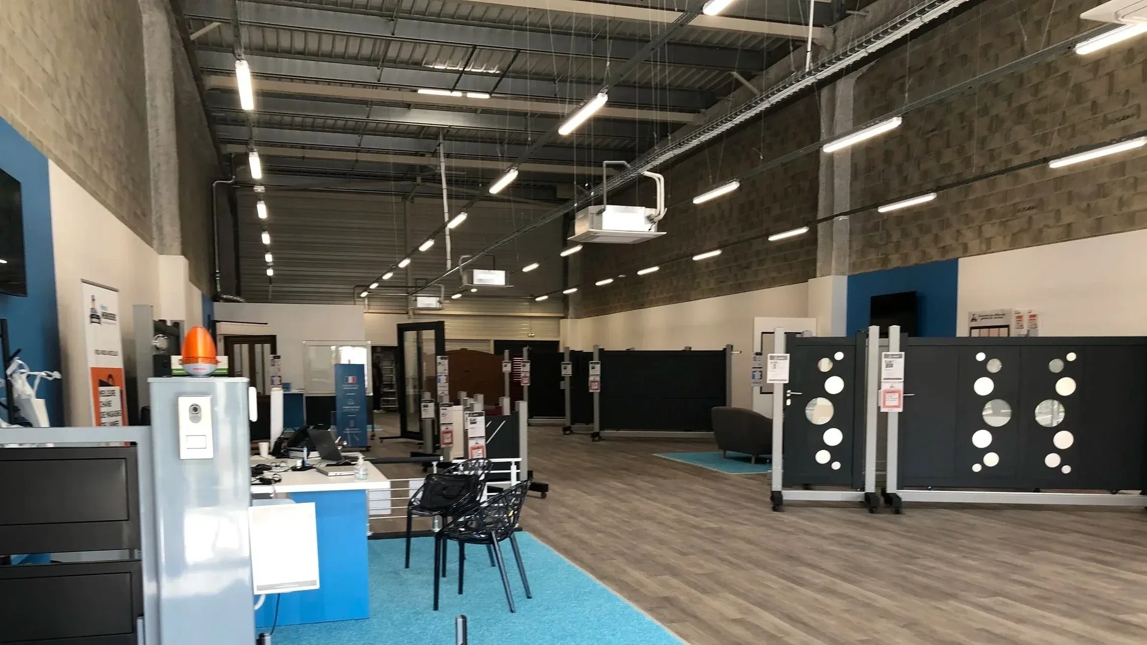 Showroom Mister Menuiserie : espace de vente avec portails, portes et fenêtres exposés et accueil bleu
